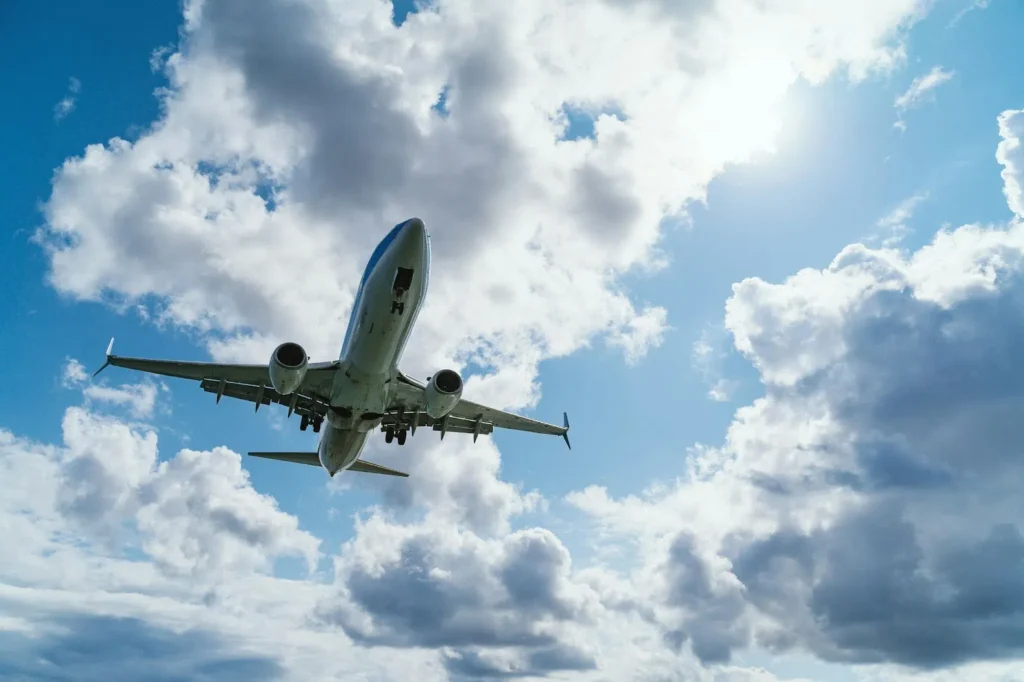 A commercial airplane flying low against a backdrop of blue sky and fluffy white clouds.