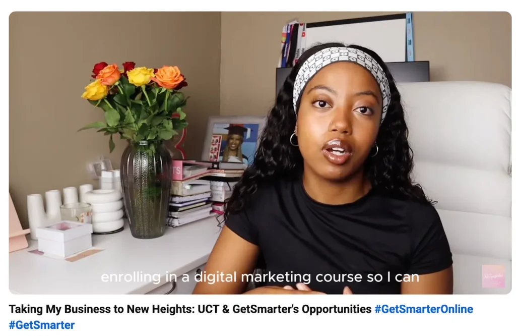 A woman in a black t-shirt sits at a desk with books and stationery, accompanied by a vibrant floral arrangement.