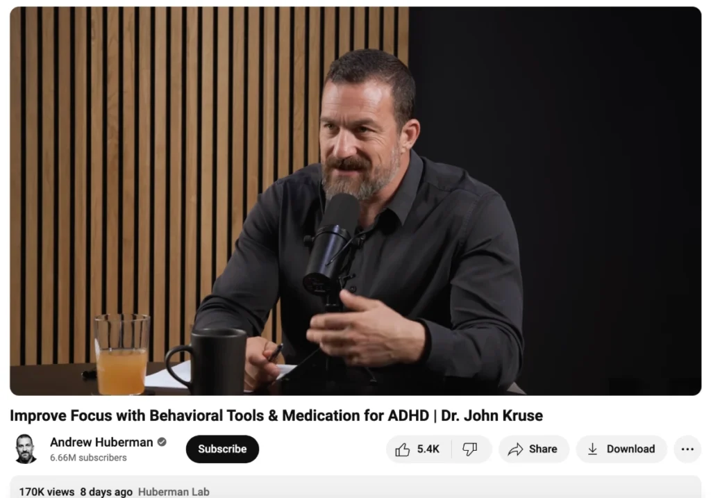 A podcast host sits at a desk with a microphone, discussing ADHD, with drinks and notes visible in a modern studio setting.