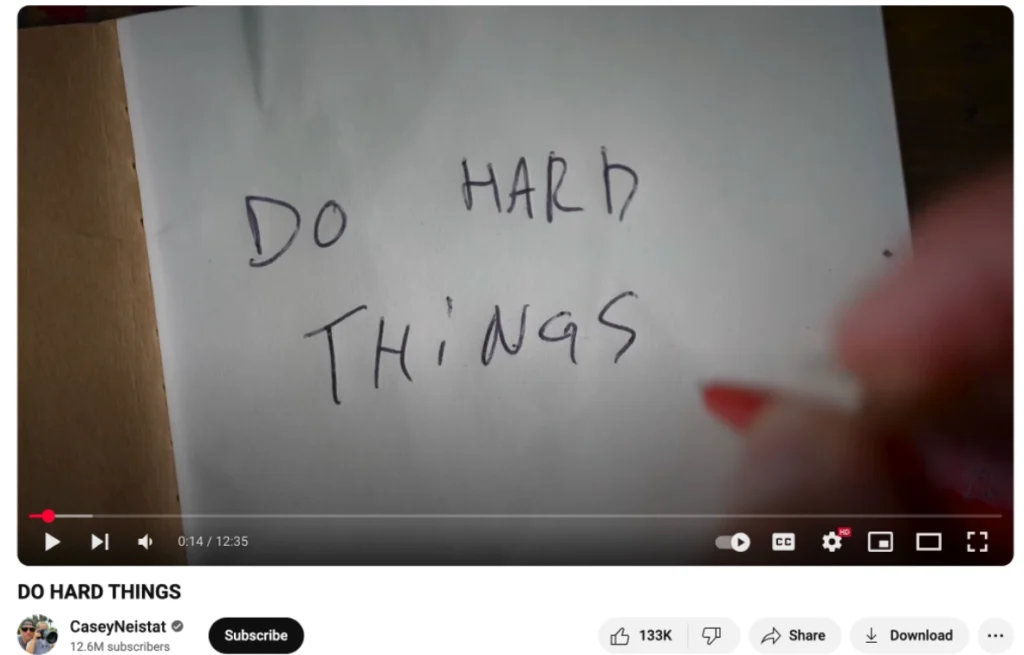 A handwritten note on a white sheet reads "DO HARD THINGS," accompanied by a hand with a red pen in the corner of the frame.