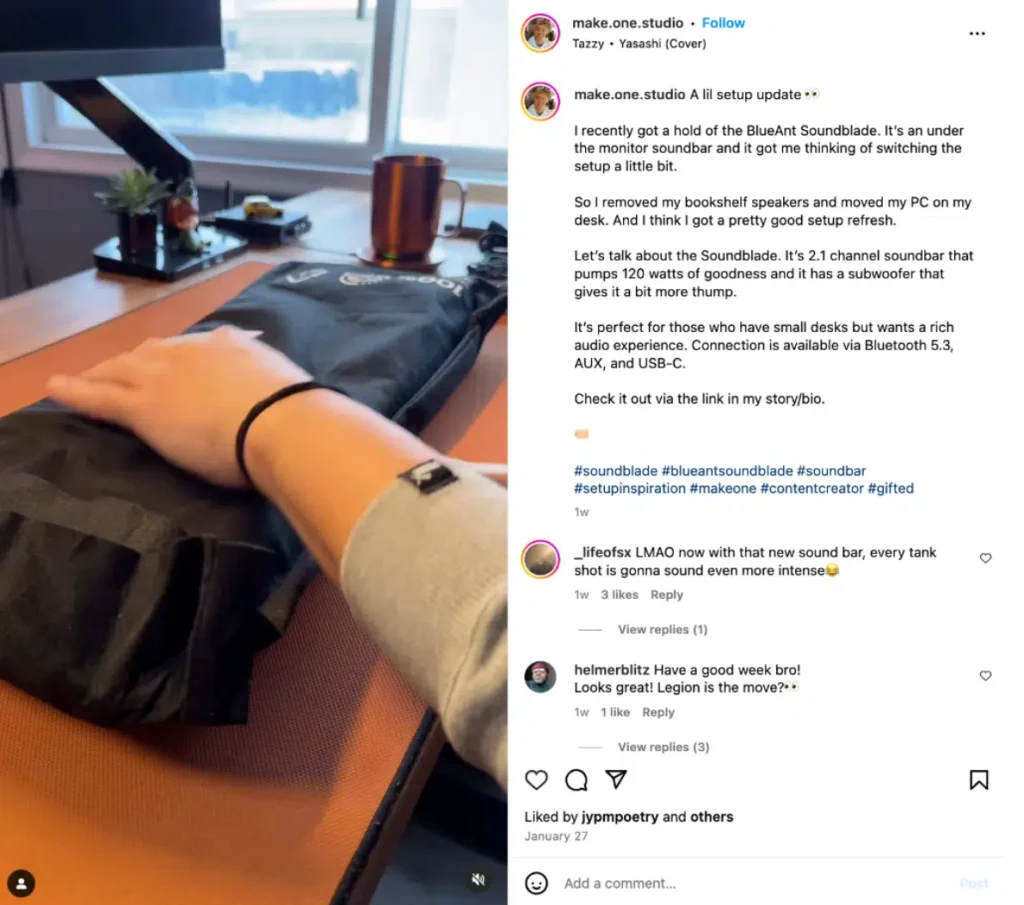 A hand rests on a sleek, black soundbar, set on a wooden desk with a coffee mug and monitor in the background, hinting at a tech refresh.