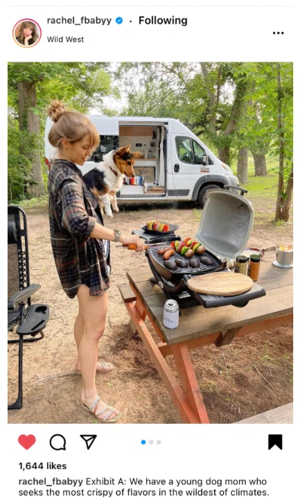 A woman in a plaid shirt cooks on a grill outdoors, with fresh vegetables and a camper van visible in the background.