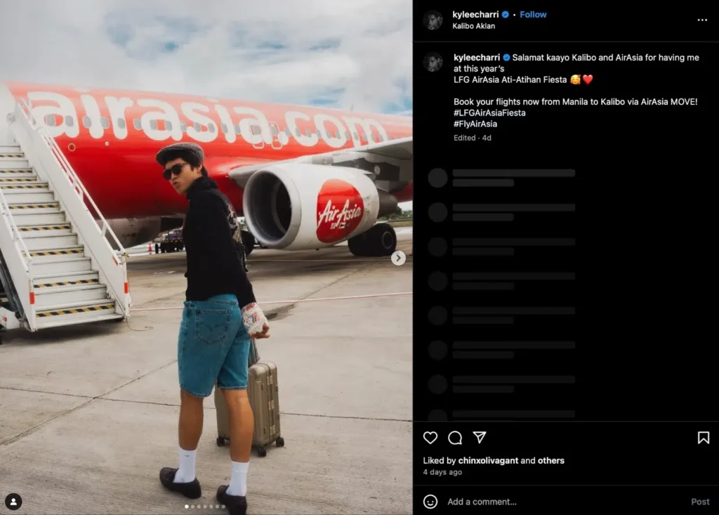 A traveler walks towards an AirAsia jet with a suitcase, wearing denim shorts and a black sweater at the airport.