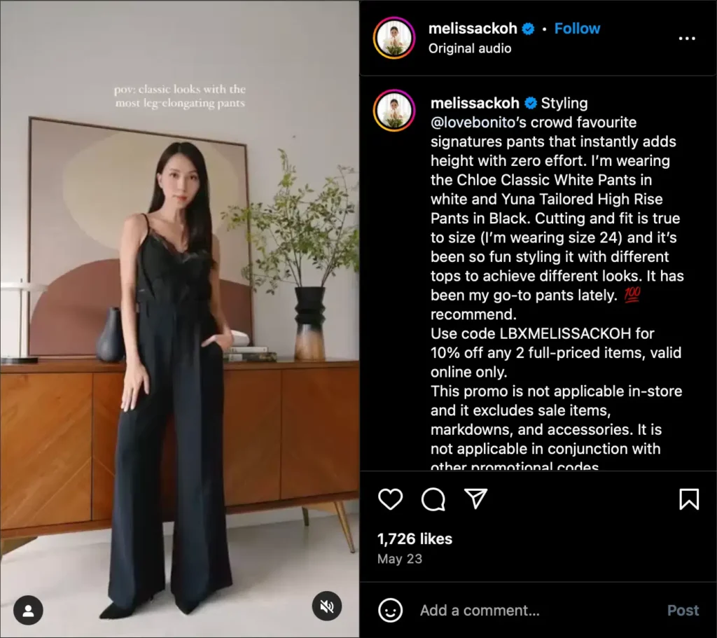 A woman poses in a stylish outfit with wide-leg pants, set against a minimalist interior featuring abstract art and greenery.