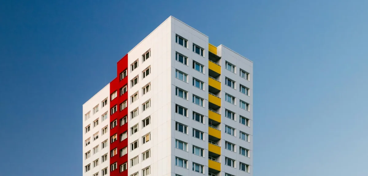 A modern residential building with white facades, a striking red section, and yellow balconies against a clear blue sky.