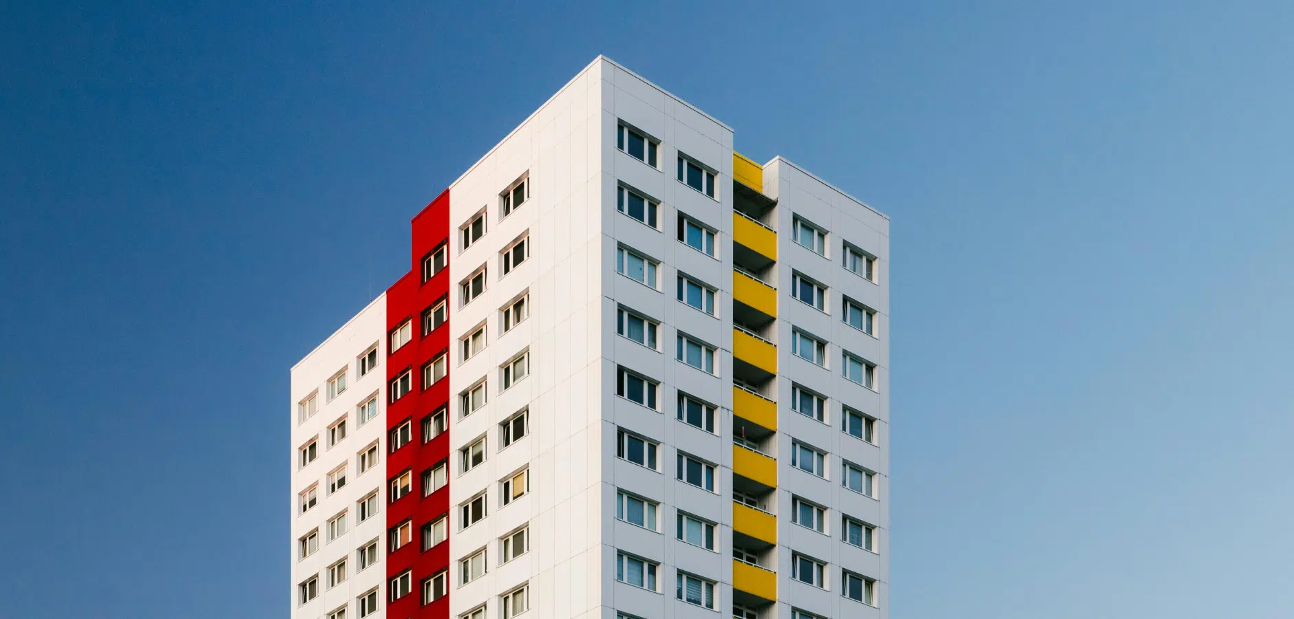 A modern residential building with white facades, a striking red section, and yellow balconies against a clear blue sky.