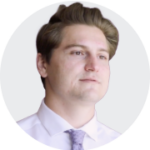 A young man in a white dress shirt and light purple tie, with a neatly styled hairstyle, set against a plain background.