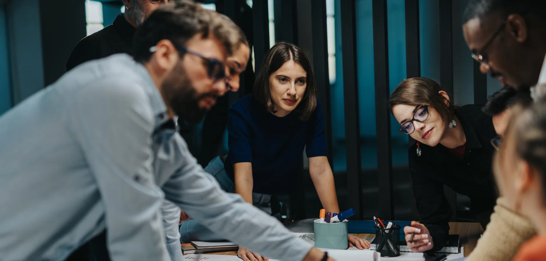 A group of people collaborates around a table filled with papers and office supplies, engaged in discussion and brainstorming.