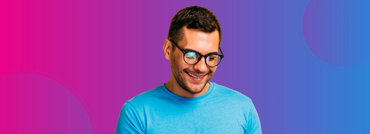 A person wearing a blue t-shirt stands against a vibrant pink to blue gradient background.