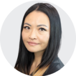 A woman with long, dark hair styled with subtle highlights, wearing a black outfit against a light gray background.