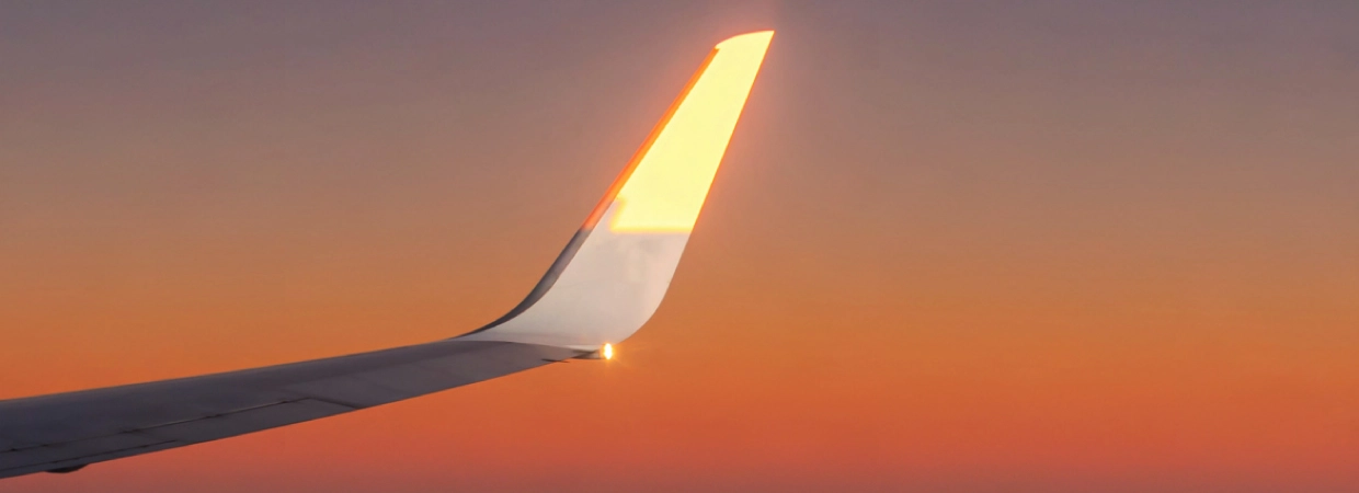 An airplane wing against a vibrant sunset, with soft oranges and purples illuminating the sky and the wingtip.