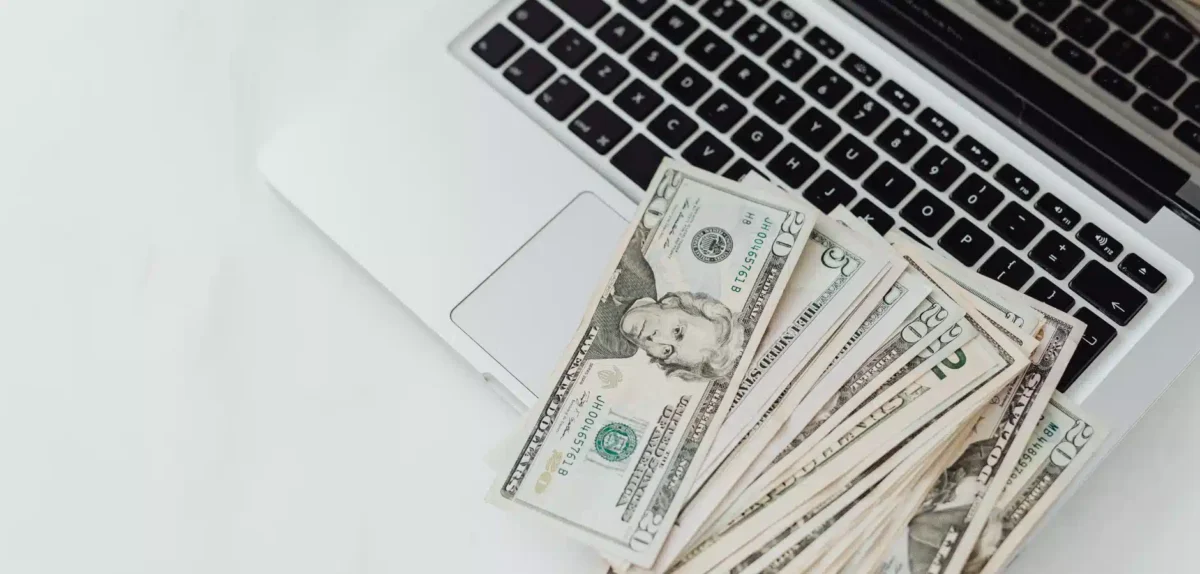 A stack of U.S. dollar bills sits atop a laptop keyboard, symbolizing online finance and digital transactions.