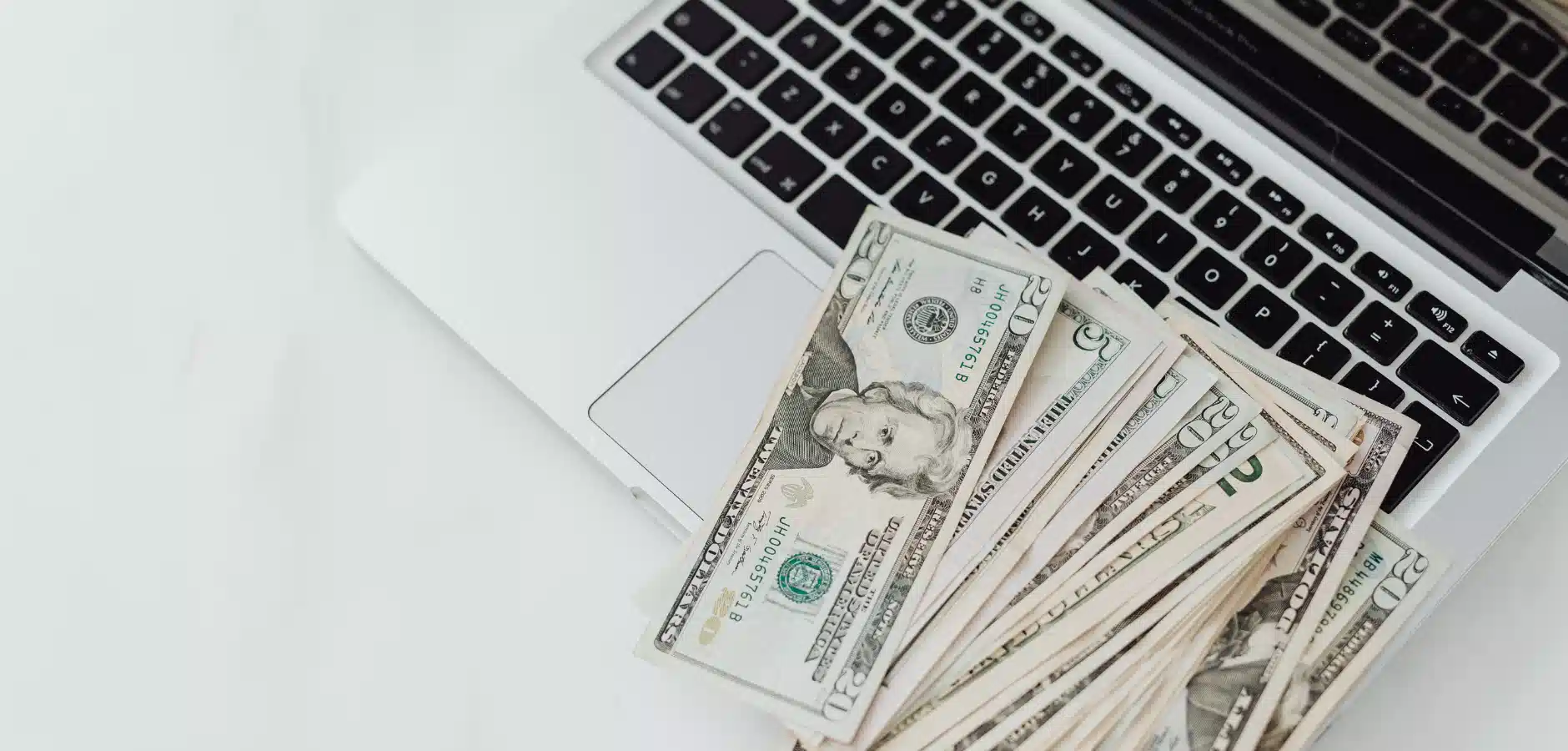 A stack of U.S. dollar bills sits atop a laptop keyboard, symbolizing online finance and digital transactions.
