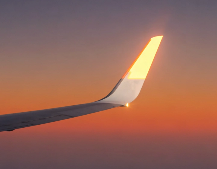 A close-up shot of an airplane wing against a vibrant sunset, with warm orange and purple hues illuminating the wingtip.
