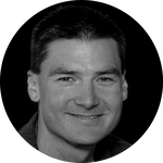 A person with short, dark hair is centered against a black background, featuring noticeable ears and a neutral expression.