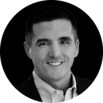 A professional portrait featuring a person in a dark suit and collared shirt, set against a black background.